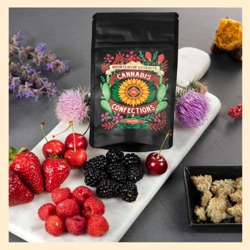 a photo of a package of edibles from Mountaintop Extracts, surrounded by various berries and cannabis buds.