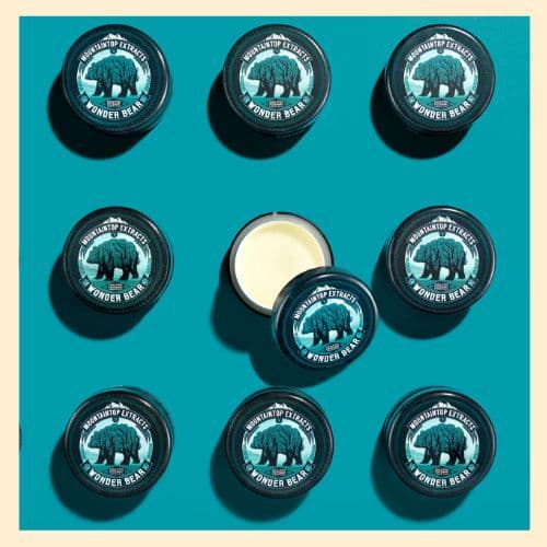 a photo of 9 tins of Mountaintop Extracts Wonderbear Salve on a blue background. One tin has the lid off so you can see the creamy salve inside. 