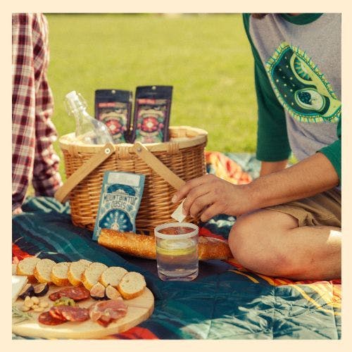 photo of two people sitting around a picnic basket with a charcuterie board and Mountaintop Extracts edibles and Oasis dissolvable powder in and next to a picnic basket.